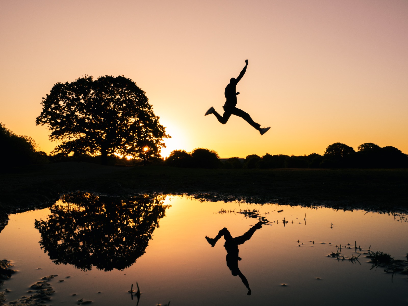 Silhouette of person jumping across stream